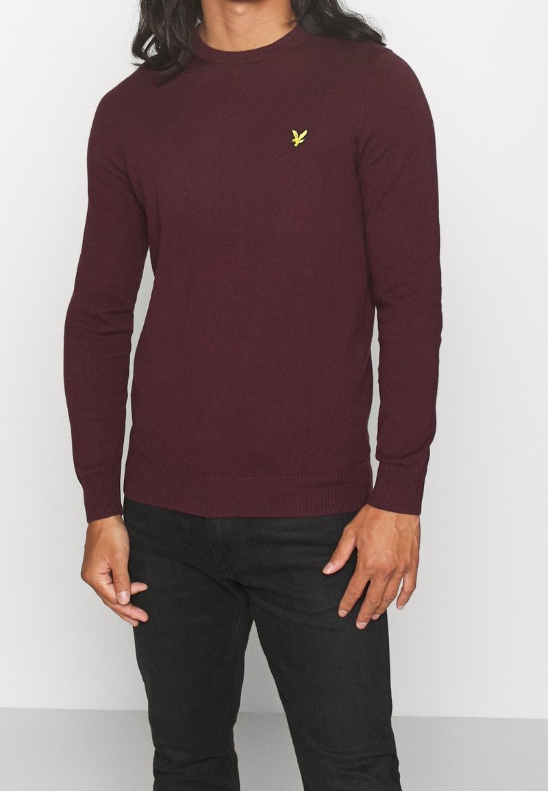 Bordeauxroter Pullover mit Rundhalsausschnitt aus strukturiertem Stoff, mit kleinem gelbem Logo auf der Brust sowie gerippten Bündchen und Saum.