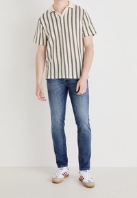 Beżowa koszulka polo z krótkim rękawem w czarne pionowe paski. W połączeniu z niebieskimi dżinsami i białymi trampkami z czerwonymi akcentami.