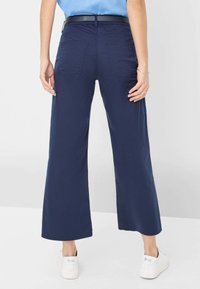 Marineblauwe wijde broek gemaakt van een soepele stof, met achterzakken en een relaxte pasvorm, gecombineerd met witte sneakers.
