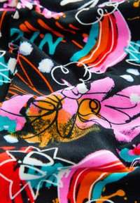 Färgglad tyg med svart bakgrund som har abstrakta blommönster i rosa, orange, turkos och vitt, med varierande texturer.