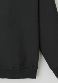 Sweatshirt noir avec une texture lisse, des poignets et un ourlet côtelés. Présente un petit logo en bas à gauche. Design simple à encolure ras du cou.