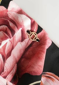 Detaliu dintr-o țesătură florală cu trandafiri mari, roz și albi, pe un fundal negru, accentuat cu un închizător circular de ton auriu.