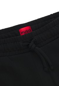 Mustat verkkarit, joissa on joustava vyötärö ja nauhakuja sekä punainen "HUGO"-logotagi. Kangas näyttää sileältä ja on yksivärinen.