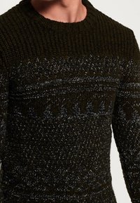 Tummanvihreä neulottu villapaita, jossa vaaleamman sävyisiä teksturoiduja kuvioita, resorilla varustettu pyöreä pääntie ja monimutkaiset silmukkakuviot.