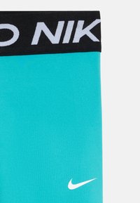 Turkusowe legginsy z czarnym pasem, na którym znajduje się napis "NIKE" w białym kolorze. Zawierają małe białe logo Nike swoosh na dolnej części przodu.