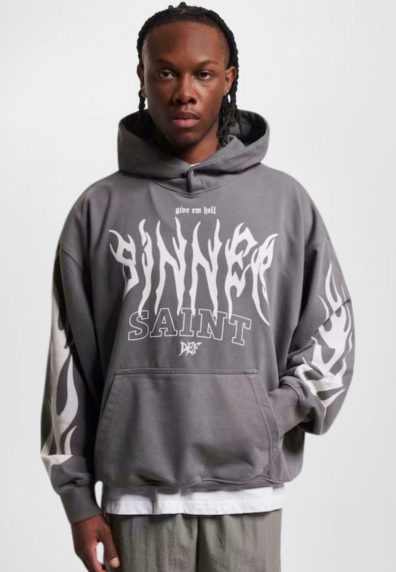Grå oversized hettegenser med frontlomme. Har fet hvit tekst "SINNER" og "SAINT," samt flammemønster på ermnene. Teksturert stoff.