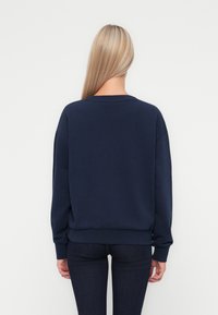 Navy blue sweatshirt with crew neck, loose fit, and long sleeves. Soft, textured fabric. Paired with dark denim jeans.