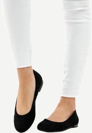 Black suede flat shoes with a rounded toe, adorned with small metallic accents. Paired with frayed hem white skinny jeans.