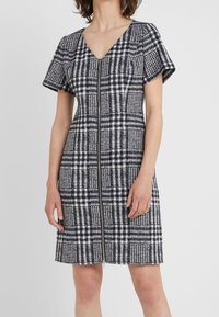 Robe à carreaux bleu marine et blanc avec manches courtes, col en V et une fermeture éclair centrale. Conçue en tissu tissé texturé, longueur jusqu'au genou.