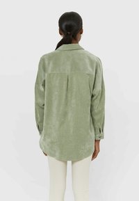 Groen ribfluwelen shirt met een rugplooie, lange mouwen en knoopmanchetten. Zachte textuur en een licht getailleerde pasvorm.