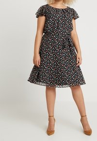 Czarna sukienka w kwiaty z krótkimi falbankowymi rękawami, dopasowanym pasem i rozkloszowaną spódnicą. Posiada małe wzory kwiatowe w kolorze białym, różowym i niebieskim.
