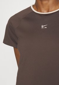 Närbild av en person som bär en brun Nike Air kortärmad tröja med en vitringad rund hals.