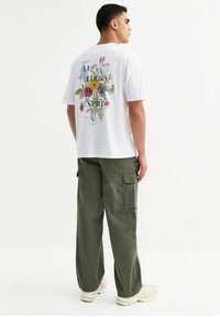 Witte t-shirt met korte mouwen, voorzien van een bloemenafbeelding en tekst op de rug; gecombineerd met losse, olijfgroene cargobroek.