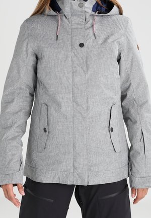 Veste à capuche gris clair avec boutons sur le devant, poches à rabat et poignets ajustables portée sur un pantalon noir.