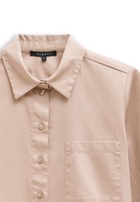 Beige Hemd mit Knöpfen und Kragen, ausgestattet mit einer Brusttasche und einer dezenten Textur. Hergestellt aus einem Stoff mit weicher Haptik. Markenlabel sichtbar.
