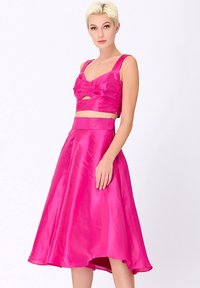 Ensemble deux pièces en satin rose comprenant un haut court avec un accent nœud et une jupe midi évasée taille haute, texture lisse et brillante.