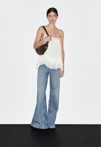 Flowy white sleeveless top with ruffle hem, paired with light blue flared jeans and a dark brown shoulder bag, against a plain background.