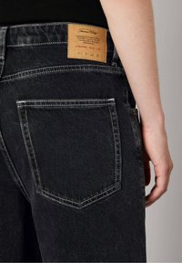 Zwarte denim jeans met een gestructureerde afwerking, featuring een bruin leren label op de tailleband en twee achterzakken met witte stiksels.