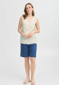 Ljust beige ärmlös topp med vertikala ränder, knappdetalj, kombinerad med mörkblå denimshorts och vita platta sandaler.