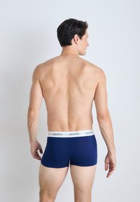 Boxer shorts bleu marine avec une ceinture élastique blanche arborant le logo Lacoste. Design ajusté en tissu lisse.