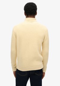 Pull en maille jaune clair avec un col haut, présentant un motif côtelé texturé. Les manches sont longues et il a un ourlet droit.