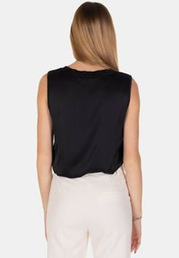 Top senza maniche nero in satin con una texture morbida, dotato di scollatura rotonda e una vestibilità morbida, abbinato a pantaloni chiari.