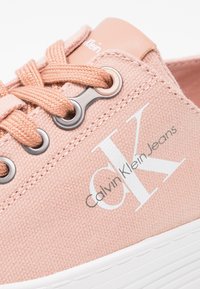 Ljusrosa canvas sneakers med vit gummisula, med runda silveröglor, beige snörning och "Calvin Klein Jeans"-logotyp i grått.