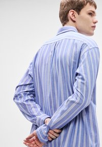 Langärmeliges Hemd in Hellblau mit weißen vertikalen Streifen. Verfügt über einen Kragen, Knopfmanschetten und eine lockere Passform. Weiche Stofftextur.