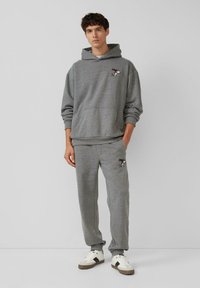 Grauer Kapuzenpullover und Jogginghose aus weicher Stoffqualität, die beide mit einer bestickten Cartoonfigur verziert sind. Mit Kapuze und Fronttasche am Kapuzenpullover.