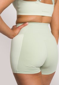 Shorts sportivi a vita alta di colore verde menta con design senza cuciture e texture liscia. Presentano un logo vicino alla vita e una tasca laterale.