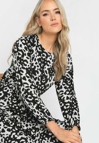 Leopardenmuster-Kleid in Schwarz und Weiß, mit langen Ärmeln, Rundhalsausschnitt und gerafften Akzenten an den Ärmeln. Glatte Stoffstruktur.