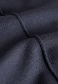 Tissu bleu marine foncé avec une texture fine en tricot, présentant une vue rapprochée des coutures surélevées et des plis délicats.