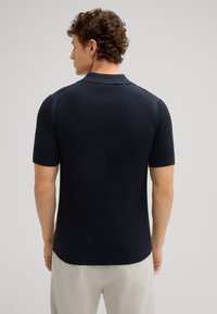 Marineblauwe gebreide poloshirt met korte mouwen en een gestructureerde stof, voorzien van een geribde kraag en zijdetails. Afgewerkt met een klein etiket.