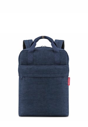 Kompakter navyblauer Stoffrucksack mit zwei oberen Griffen, gepolsterten Schulterriemen, Frontreißverschlusstasche und rotem Markenzeichen an der Seite.