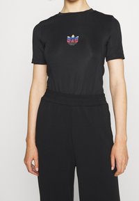 Černý bodysuit s krátkými rukávy vyrobený z pružného materiálu, který má na hrudi vícebarevné logo a elastický pas.