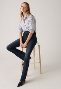 High-waisted dark denim jeans with a slight flare, paired with a white and blue striped button-up shirt. Smooth texture and tailored fit.