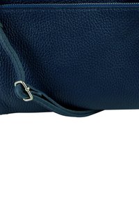 Donkere blauwe leren tas met een gestructureerd oppervlak, voorzien van een lang riempje en zilverkleurige hardware. Ritspocket bovenaan voor sluiting.