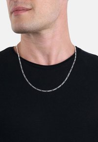 Primo piano di un uomo che indossa una collana di catena argento sopra una maglietta nera a collo rotondo, con il viso inferiore e il collo in mostra.