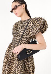 Black handbag with rectangular shape and gold hardware, held by a person wearing a leopard print dress with puffy sleeves.