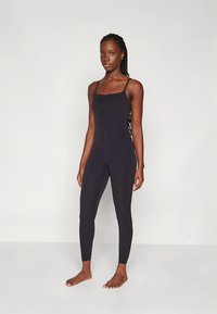 Črn, oprijemalni kombinezon s tankimi naramnicami, z gladko teksturo in brezšivno zasnovo, primeren za različne dejavnosti.