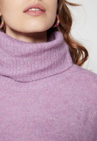 Pull en col roulé de couleur violet clair, fabriqué en tissu tricoté doux et texturé, avec un large col et un subtil effet mélangé.