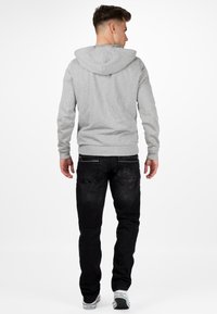 Felpa grigia con tasca a marsupio, polsini e orlo a costine. Abbinata a jeans neri con tasche sul retro e una texture sbiadita. Sneakers bianche.