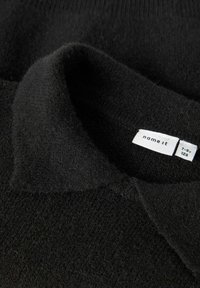 Schwarzer Strickpullover mit weicher Textur und umgeschlagenem Kragen. Etikett sichtbar mit dem Markennamen "name it" und Größeninformationen.