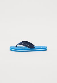 Marine flip-flops med en teksturert stropp og blå såle, med et mønster av små, fargerike nautiske motiver på sålen. Merkevarelogo tilstede.