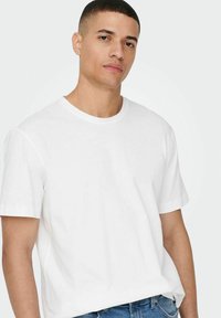 White cotton t-shirt with a round neckline and short sleeves, featuring a relaxed fit. Worn with blue denim jeans.