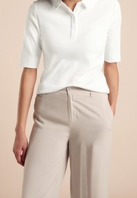 Vit kortärmad pikétröja med krage, tillsammans med ljusbeiga byxor med knappstängning och sidofickor. Släta ytor.