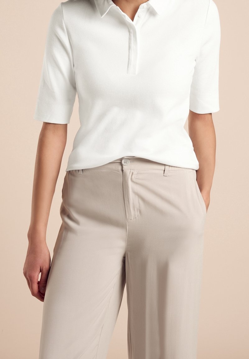 Vit kortärmad pikétröja med krage, tillsammans med ljusbeiga byxor med knappstängning och sidofickor. Släta ytor.