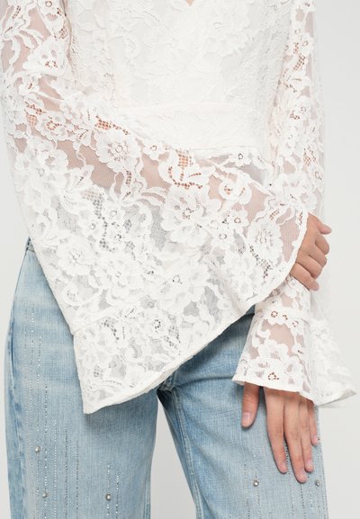 Witte kanten top met uitlopende lange mouwen, ingewikkelde bloemenpatronen, gecombineerd met lichtblauwe denim met subtiele versieringen.