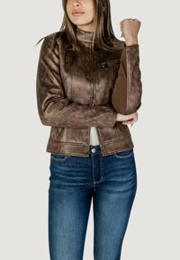 Giacca in finta pelle marrone con collo alto, tasca con zip e dettagli a coste, abbinata a jeans in denim blu.