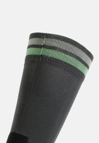 Calzino nero con una superficie testurizzata, caratterizzato da strisce grigie e verdi sulla parte superiore, progettato per comfort e durata.